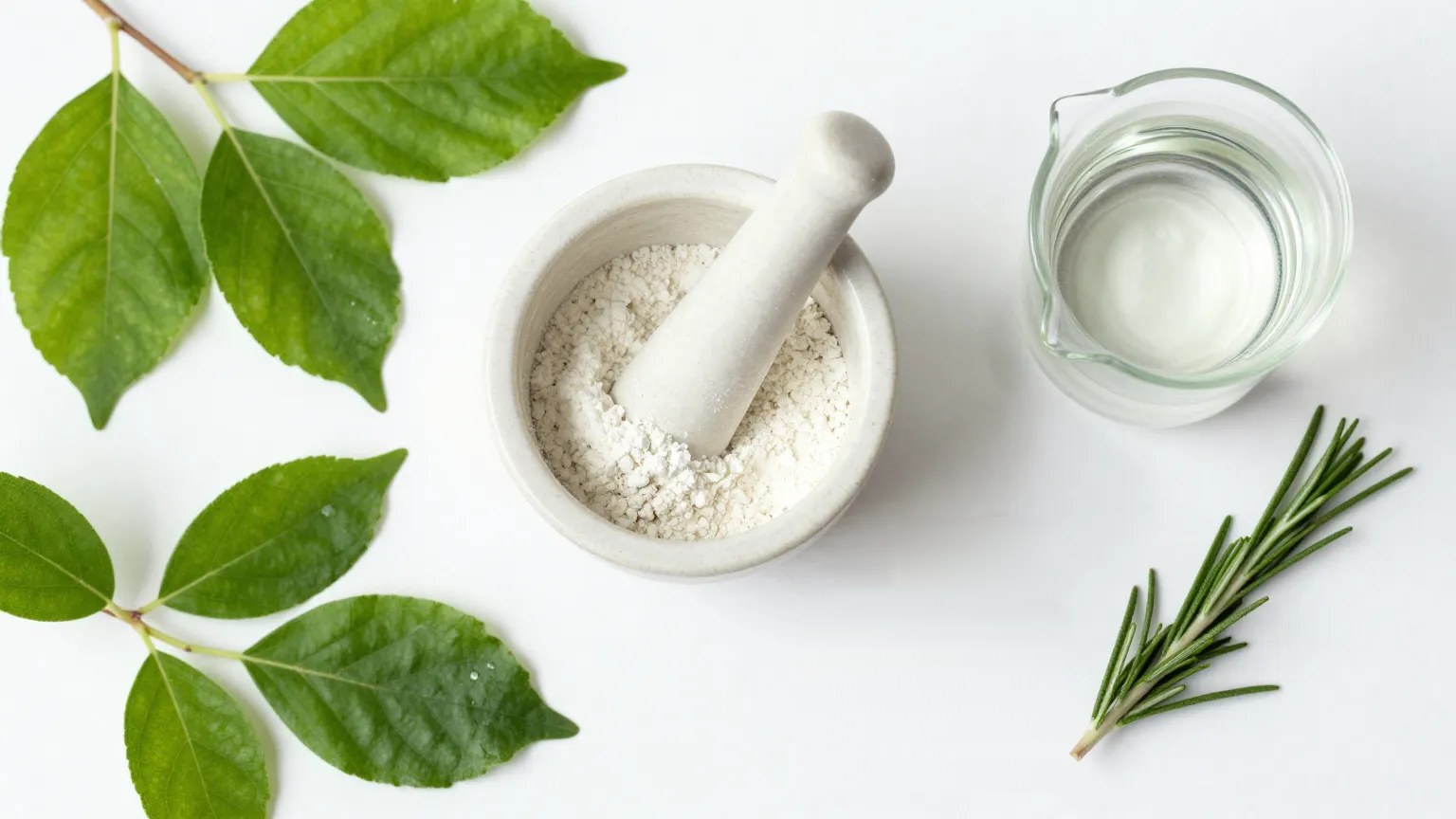 Mortar and pestle with fresh green leaves and rosemary on a white bench